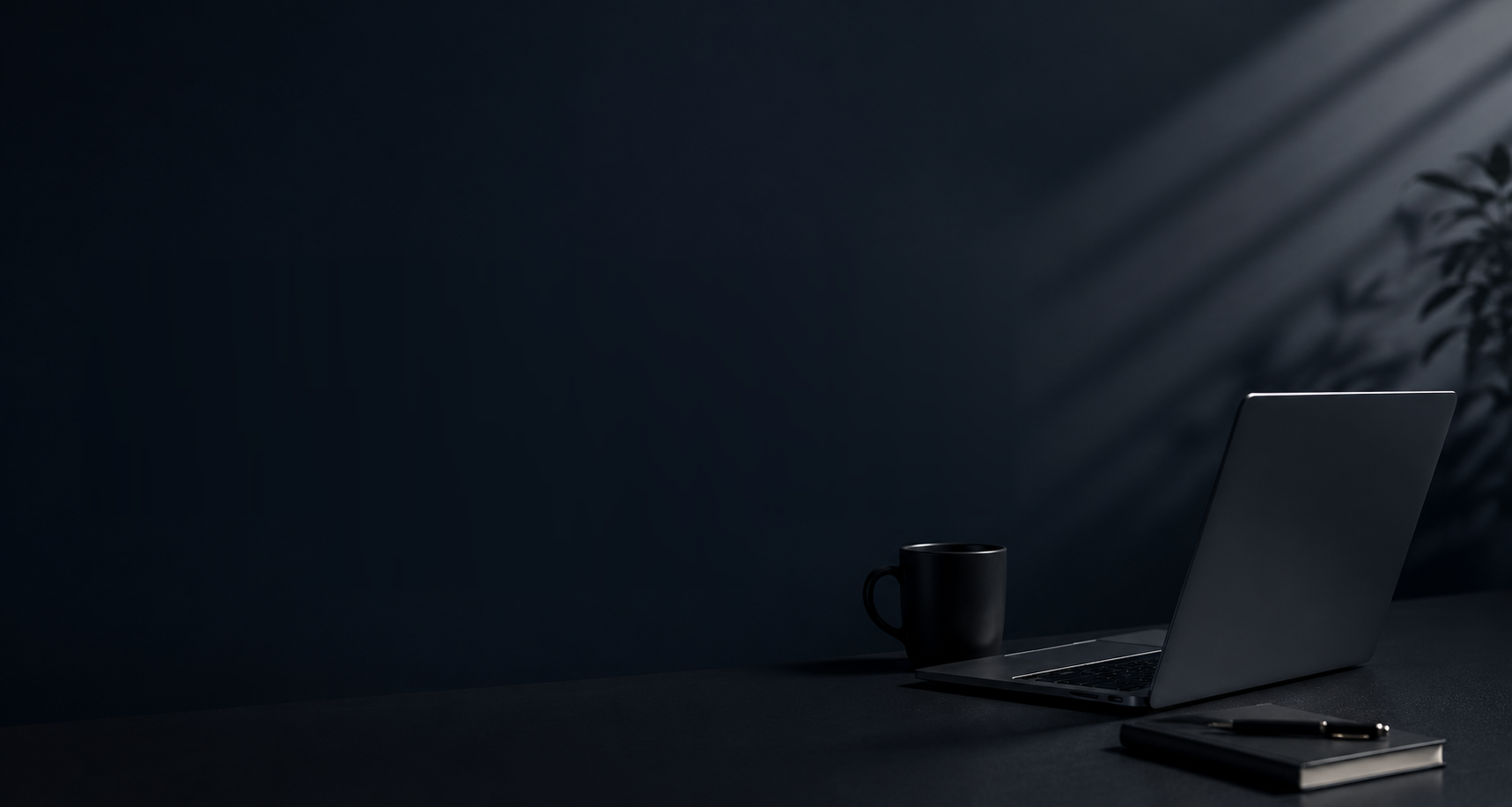 A modern, minimal workspace — laptop, coffee, and notebook on a dark desk