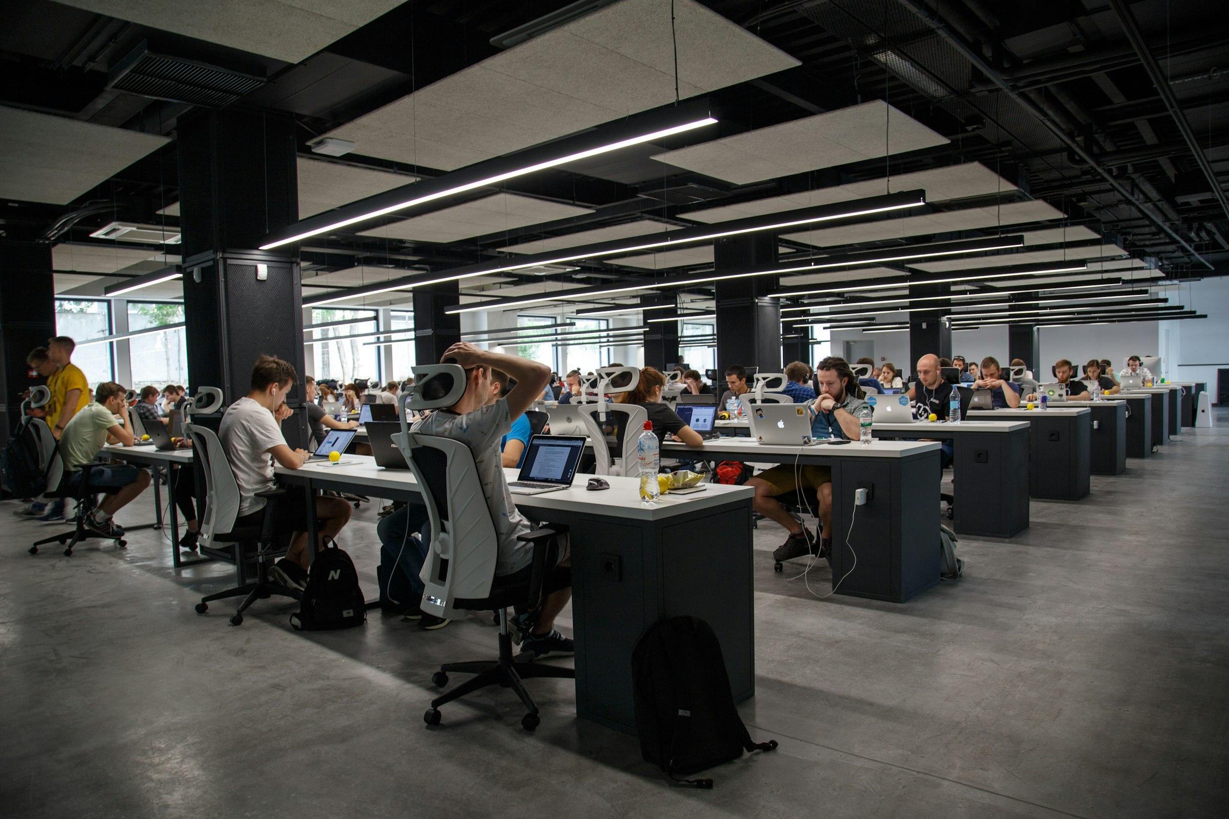 Open-plan office full of people working laptops — the manual reporting grind